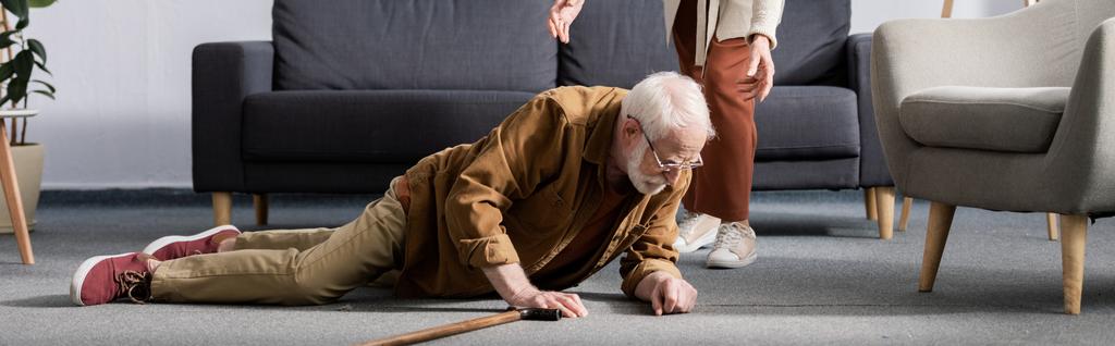 Teilansicht einer Frau, die einem gestürzten älteren Mann hilft, vom Boden aufzustehen, horizontales Konzept - Foto, Bild