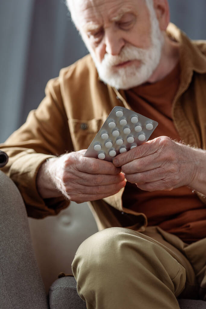 Selektiver Fokus einsamer älterer Mann, der sich schlecht fühlt und Tabletten in der Hand hält - Foto, Bild
