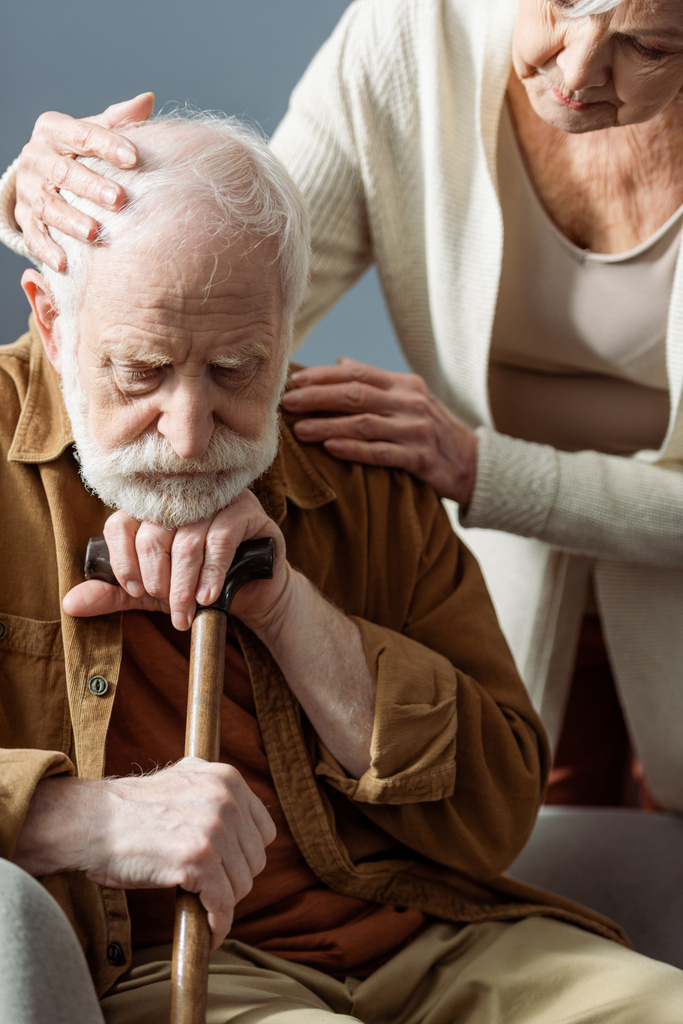 ηλικιωμένη γυναίκα ηρεμεί άρρωστο γέρο σύζυγο, άρρωστος στην άνοια, ενώ αγγίζει το κεφάλι και τον ώμο του  - Φωτογραφία, εικόνα