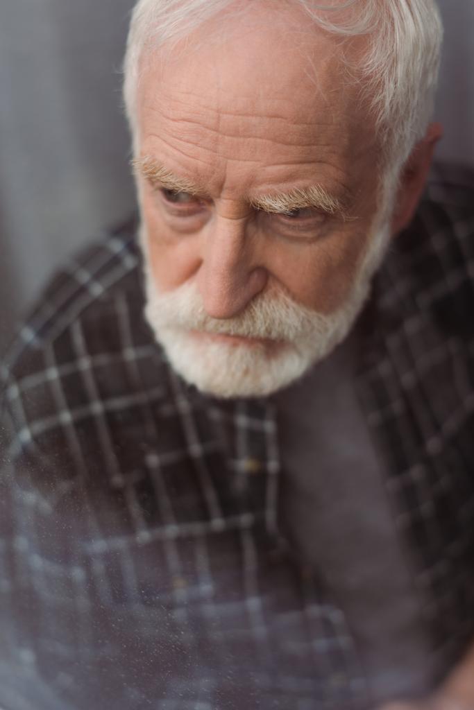 вибірковий фокус пригніченого старшого чоловіка, який дивиться далеко через віконне скло
 - Фото, зображення