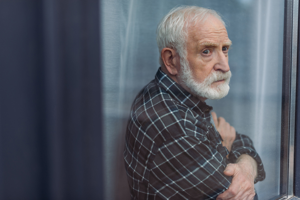 starší, rozrušený muž stojící se zkříženýma rukama a dívající se oknem - Fotografie, Obrázek