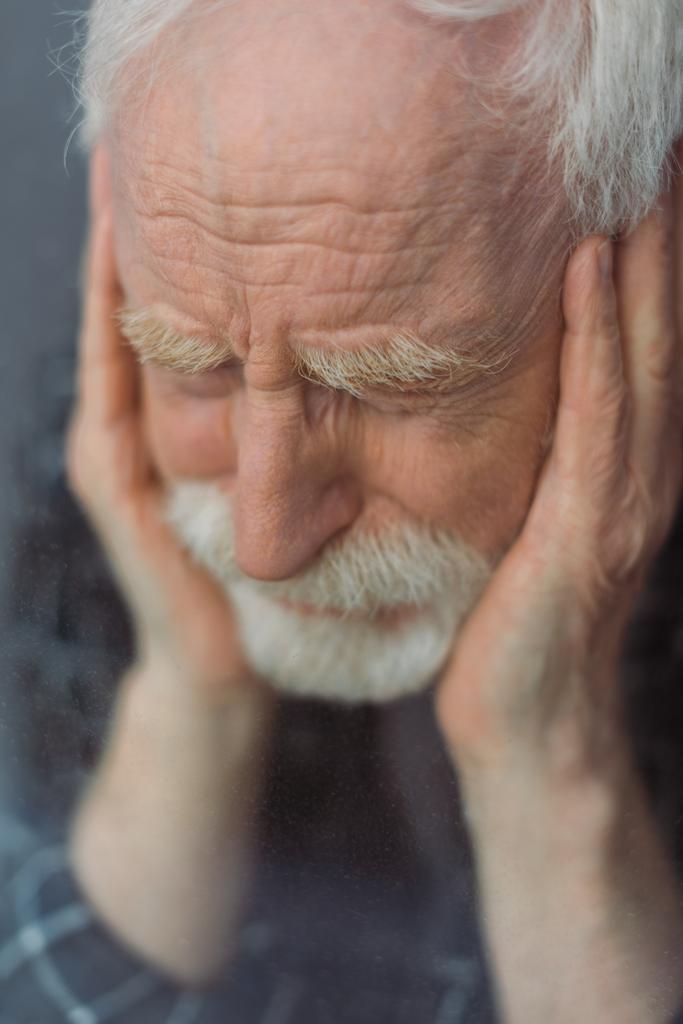 foyer sélectif de l'homme âgé, déprimé avec les yeux fermés touchant le visage près du verre de fenêtre - Photo, image
