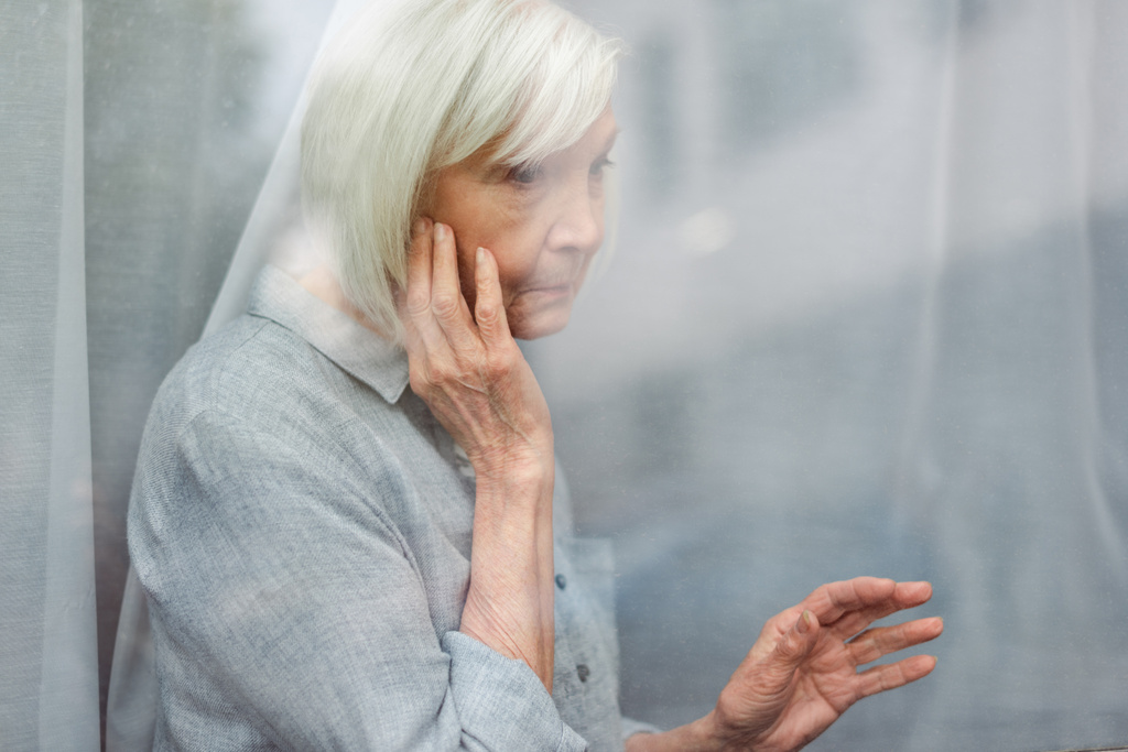 depressziós idős nő megható arc és ablak üveg, miközben félrenéz - Fotó, kép