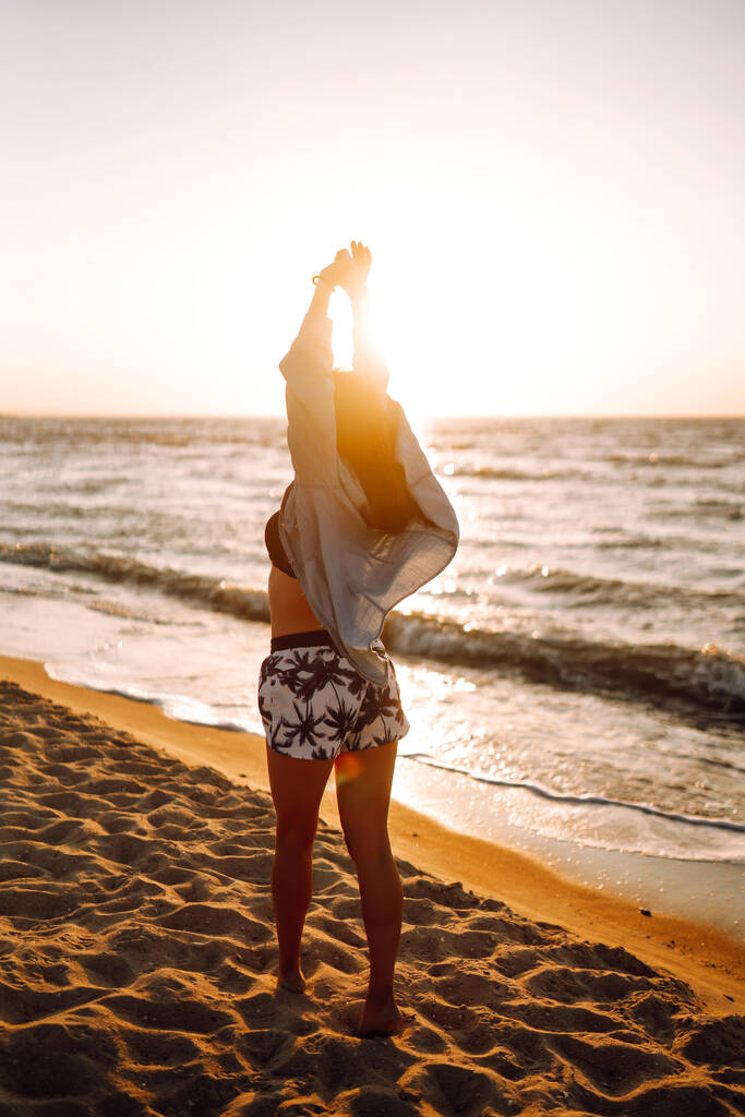 Дівчина насолоджується відпочинком на пляжі на заході сонця. Концепція відпочинку, подорожей, свободи та літніх канікул
. - Фото, зображення