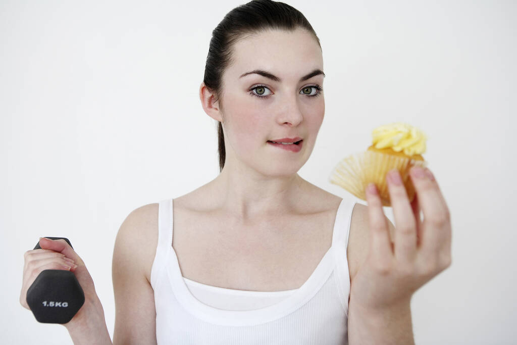 Femme manger cupcake tout en soulevant haltère - Photo, image