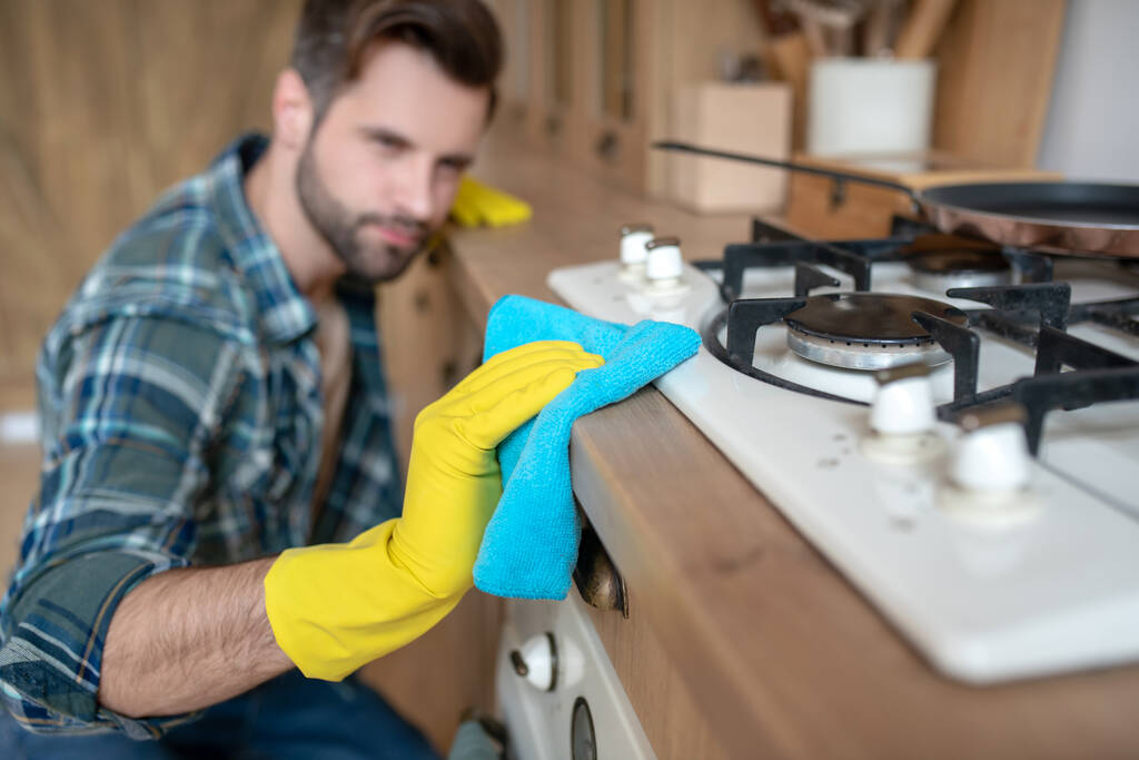 Hombre con guantes amarillos limpiando la superficie de la cocina
 - Foto, Imagen