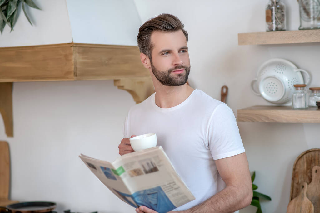 Μελαχρινός όμορφος άντρας που κρατάει εφημερίδα και πίνει καφέ. - Φωτογραφία, εικόνα