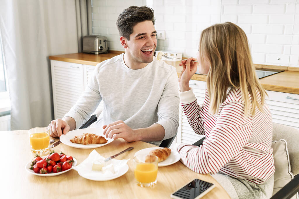 Portré fiatal boldog pár eszik együtt az asztalnál, miközben a reggeli a hangulatos konyhában otthon - Fotó, kép