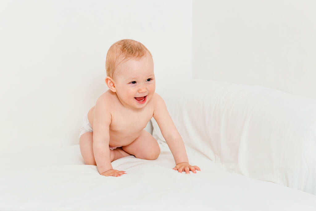 Hilariante bebê de dez meses de idade em uma fralda rasteja na cama
 - Foto, Imagem