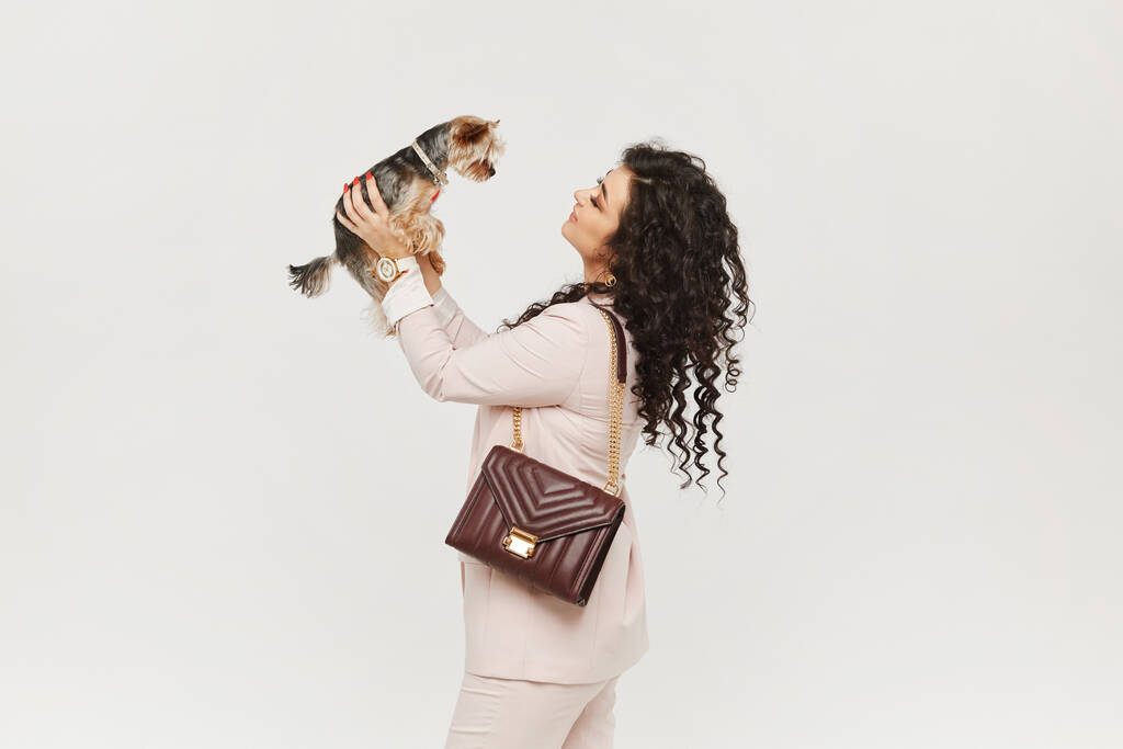 Μια νεαρή γυναίκα σε ένα μπεζ κοστούμι κρατώντας Yorkie Terrier στα χέρια και θέτουν στο λευκό φόντο, απομονώνονται με αντίγραφο χώρο. - Φωτογραφία, εικόνα