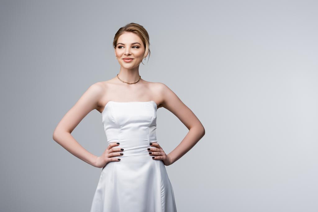 グレーで隔離された腰の上に手を置いて立っているウェディングドレスの陽気な花嫁  - 写真・画像