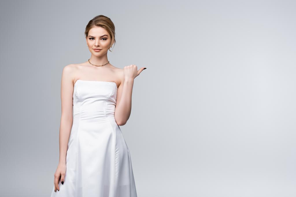 Verwirrte Braut im weißen Brautkleid zeigt mit Daumen auf Grau  - Foto, Bild