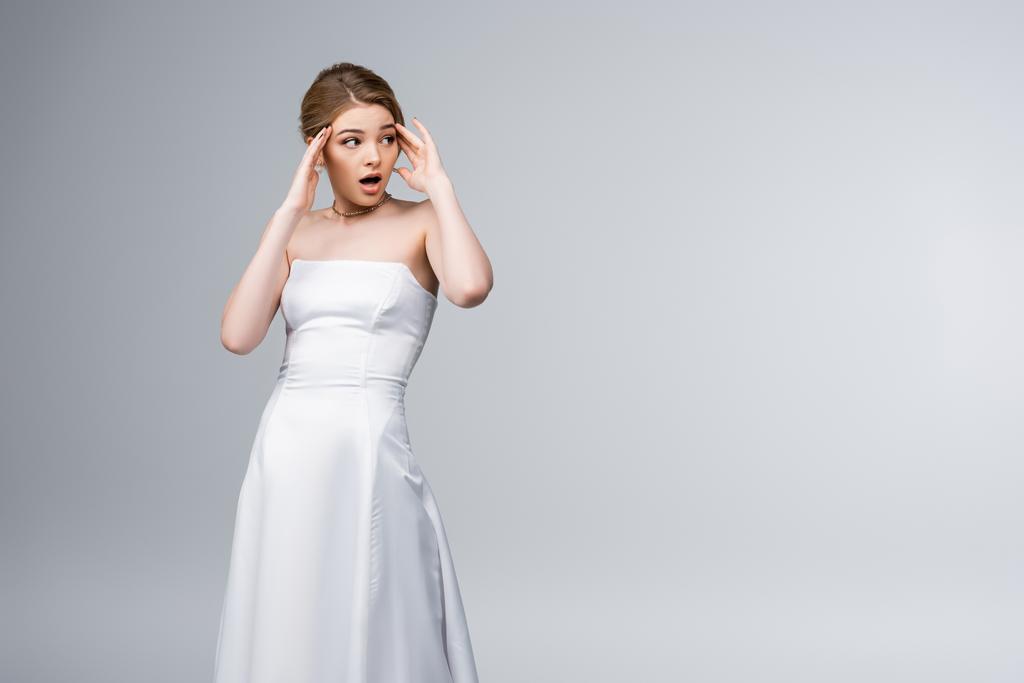 shocked girl in wedding dress looking away and touching temples isolated on grey  - Photo, Image