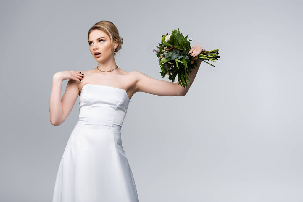 noiva insatisfeita em vestido branco segurando buquê de flores isoladas em cinza
  - Foto, Imagem