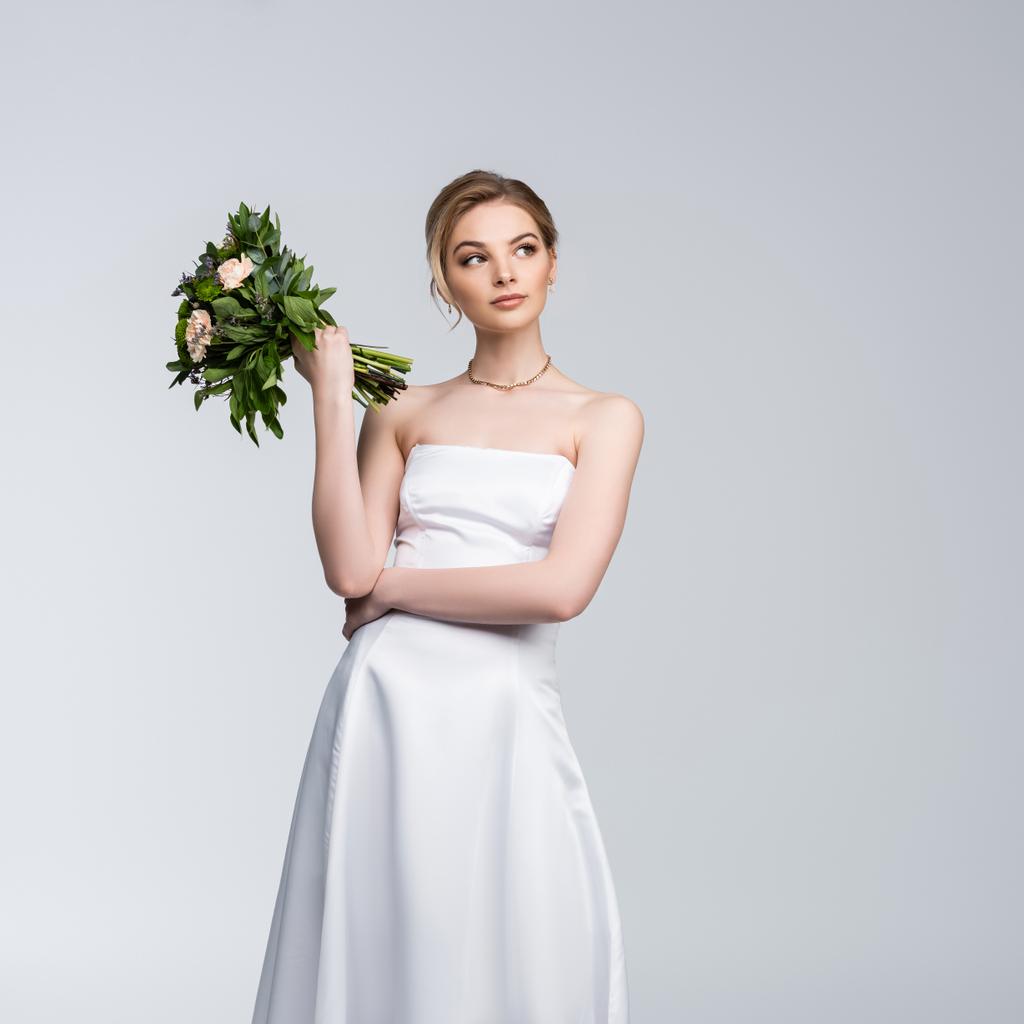 fille coûteuse en robe de mariée blanche tenant bouquet de fleurs isolées sur gris  - Photo, image