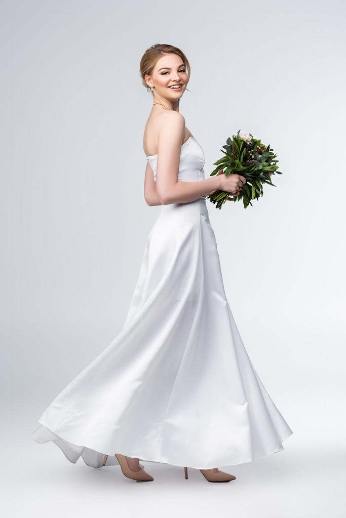 novia sonriente en elegante vestido de novia con ramo de flores en gris
  - Foto, Imagen