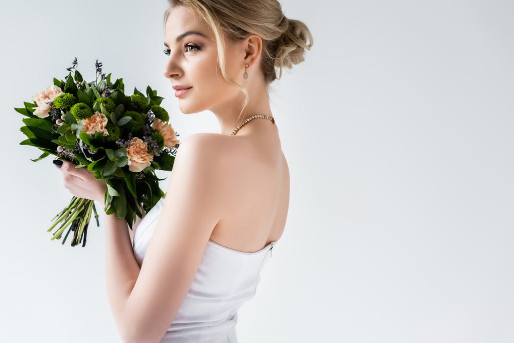 atraktivní nevěsta ve svatebních šatech drží květiny na bílém  - Fotografie, Obrázek