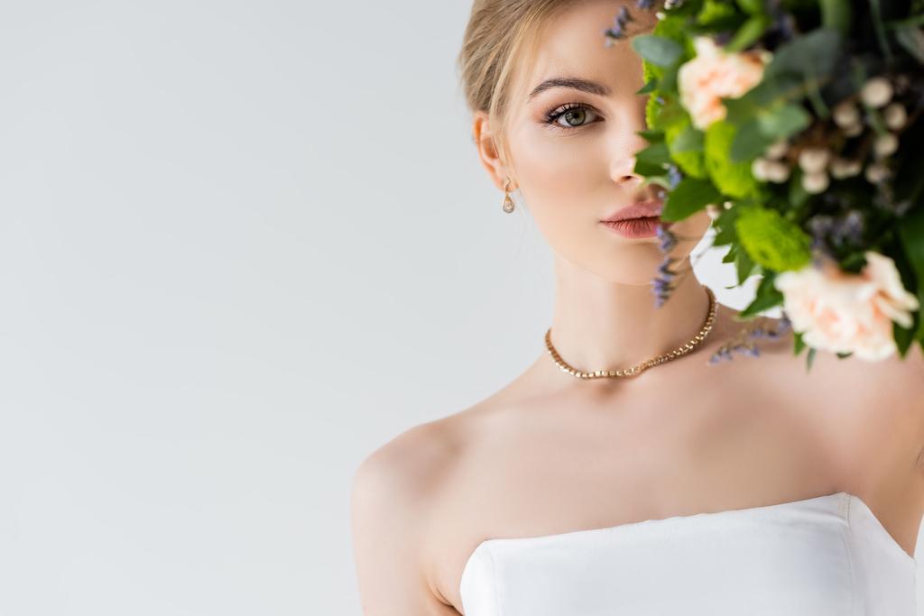 schöne Braut im eleganten Hochzeitskleid, das Gesicht mit Blumen auf Weiß verdeckt  - Foto, Bild