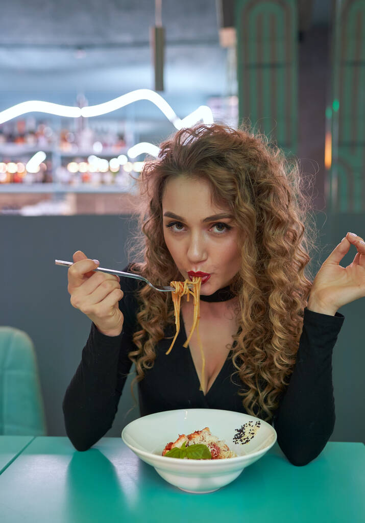 Cute girl with curly hair eating pasta in a restaurant. - Photo, Image