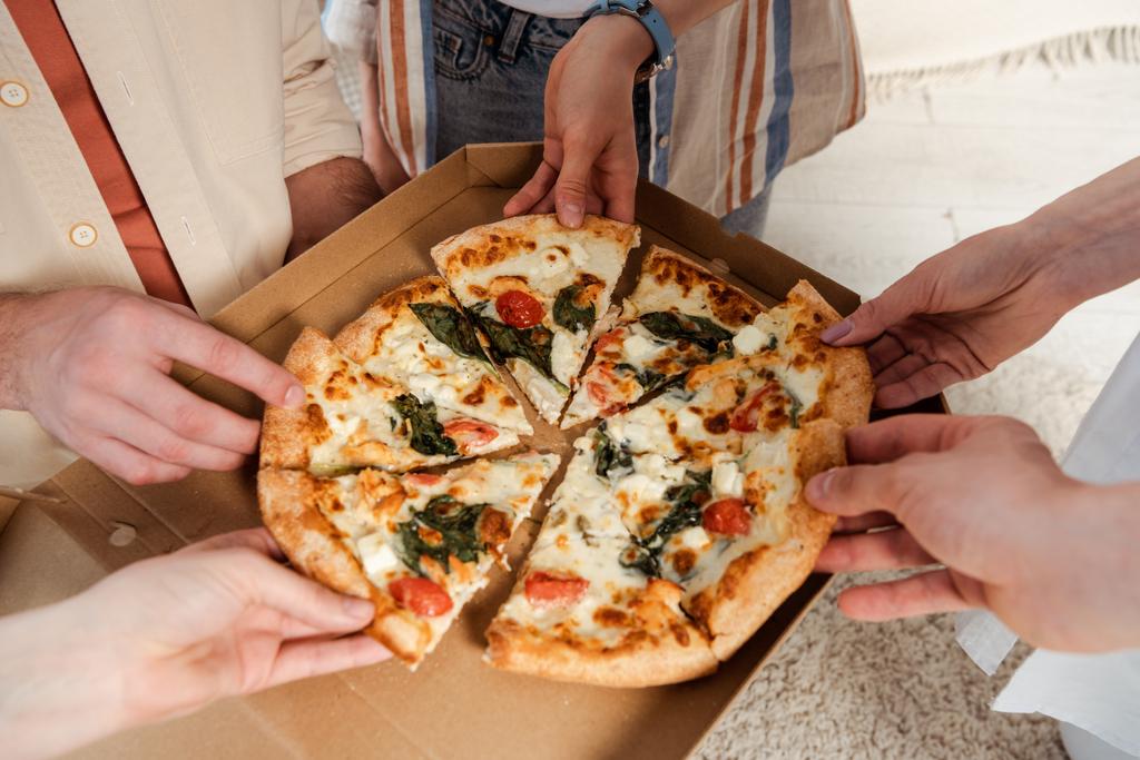 Ausgeschnittene Ansicht von Freunden, die Stücke leckerer Pizza zu Hause halten - Foto, Bild