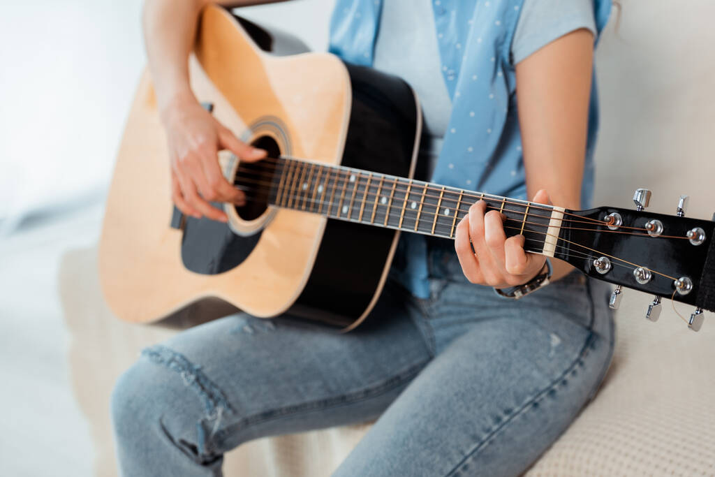 Ausgeschnittene Ansicht einer jungen Frau mit Akustikgitarre auf dem Sofa  - Foto, Bild