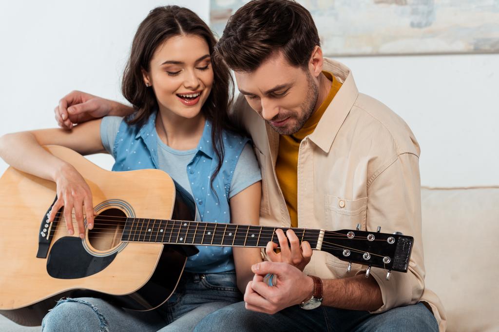 Homme embrassant petite amie souriante tout en jouant de la guitare acoustique ensemble - Photo, image