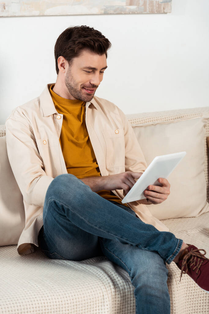 Schöner Mann mit digitalem Tablet auf Couch im Wohnzimmer - Foto, Bild