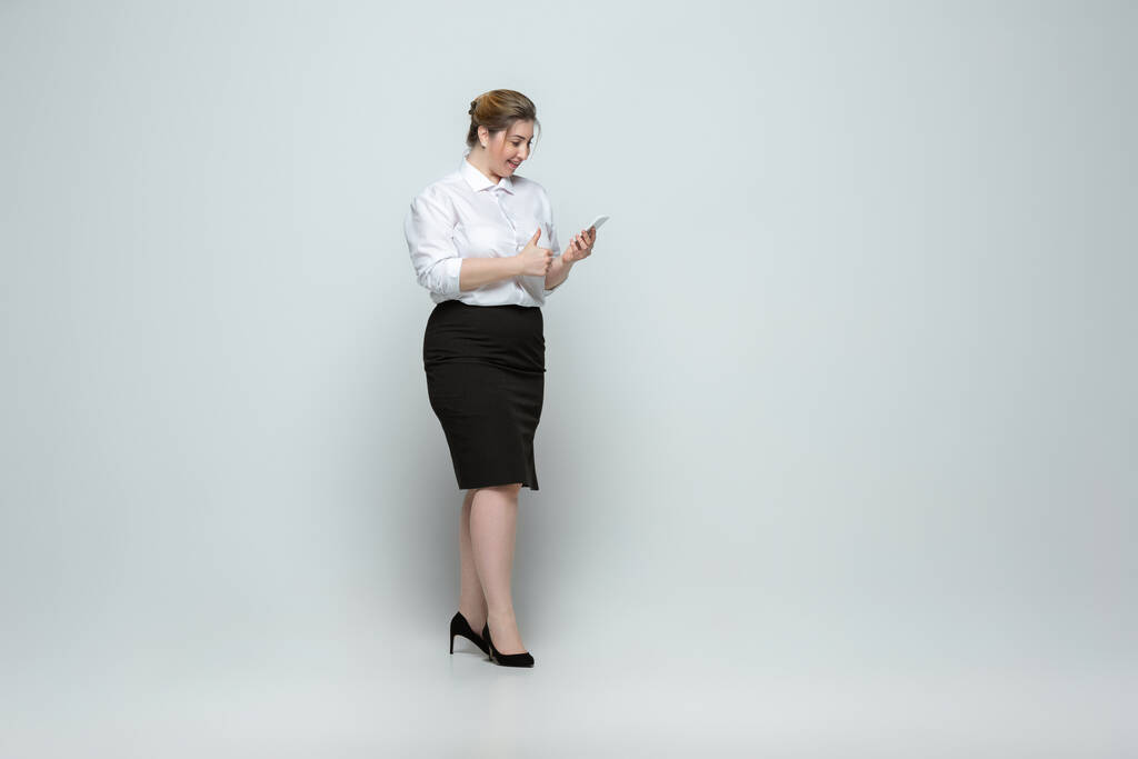 Jonge blanke vrouw in kantoor kledij op grijze achtergrond. Lichaamspositief vrouwelijk karakter. plus grootte zakenvrouw - Foto, afbeelding