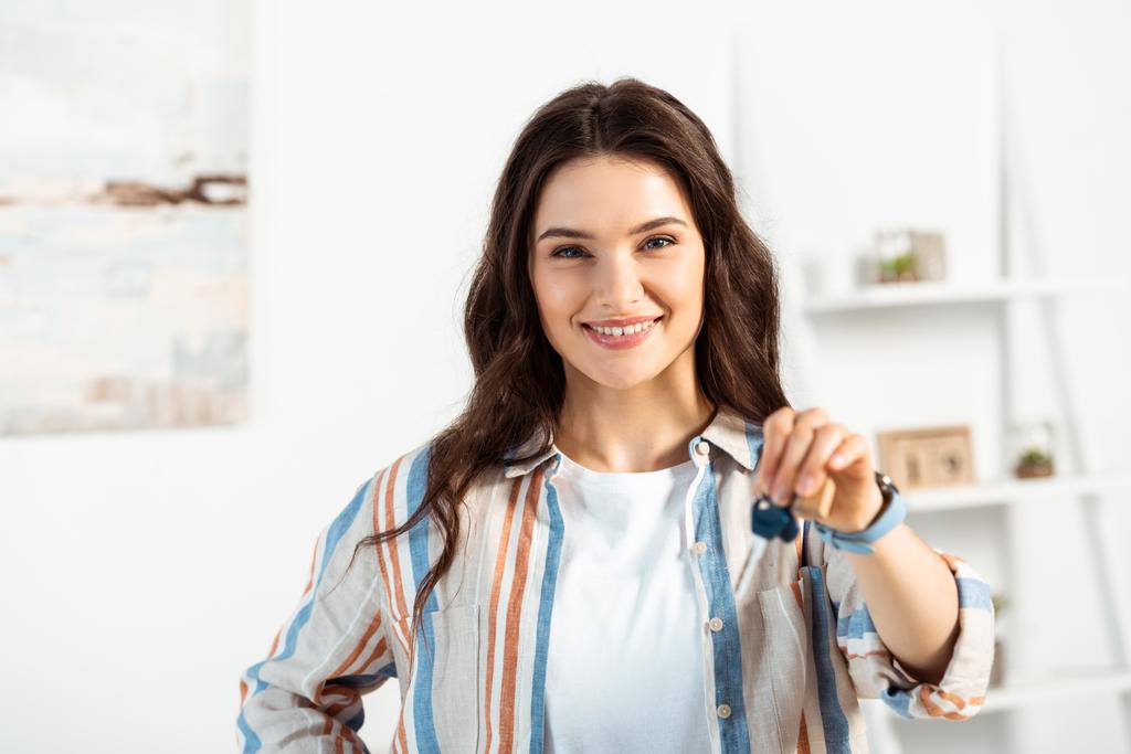 Selective focus of smiling woman holding keys of new house in living room - Photo, Image