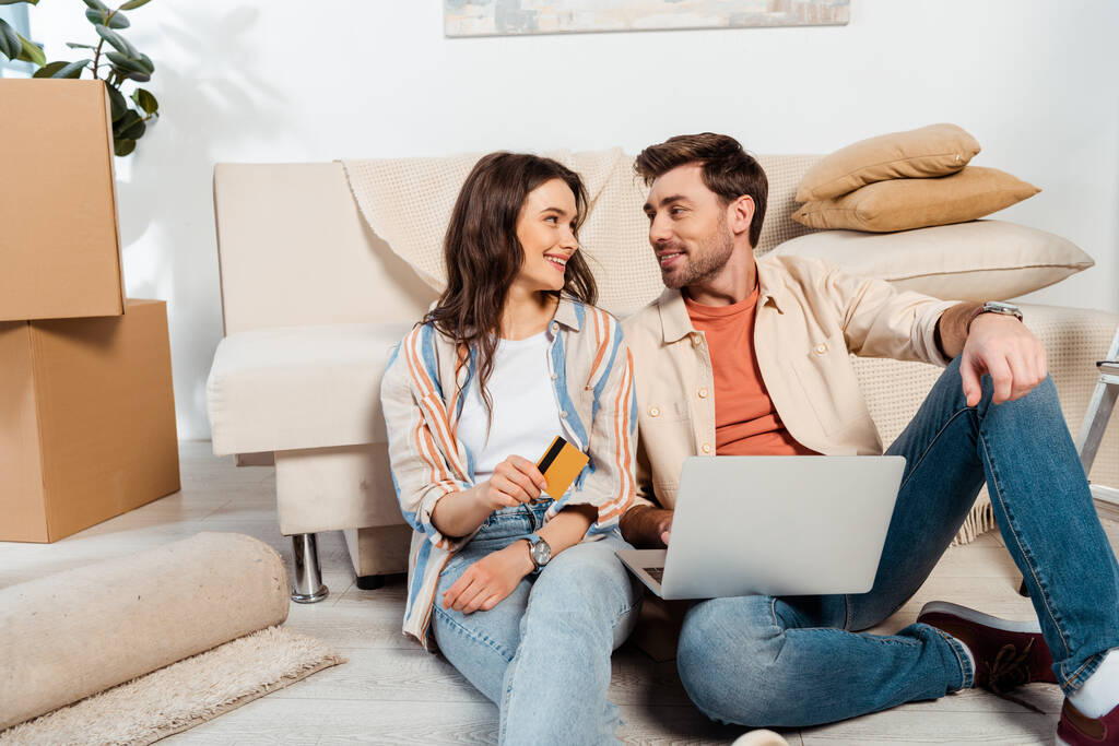 Smiling couple using laptop and credit card on floor during moving  - Photo, Image