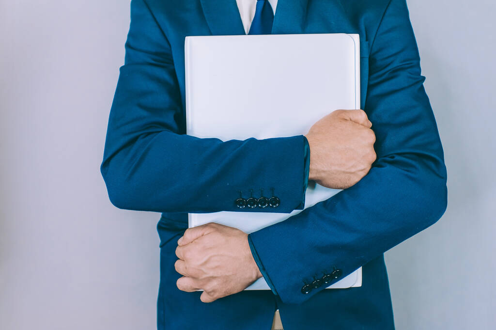 Zakenman met een blauwe jas op een grijze achtergrond met een laptop in zijn handen - Foto, afbeelding