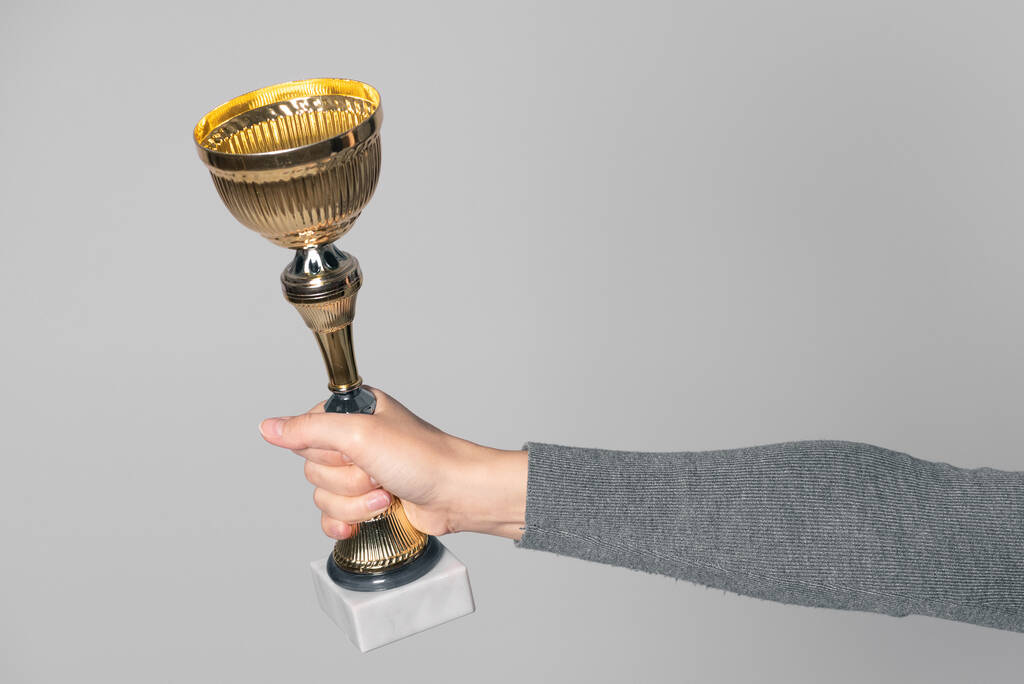 Golden award cup in winnaar hand geïsoleerd op grijze achtergrond. Uitreiking. - Foto, afbeelding