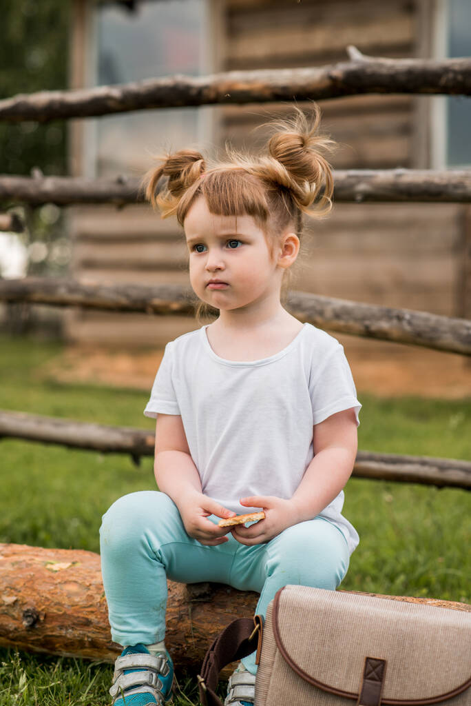 szabadtéri portré egy lányról, aki a fűben ül a kerítés mellett.Nyár a faluban. gyönyörű kislány egy fa bench.ecology és boldog gyermekkort. - Fotó, kép