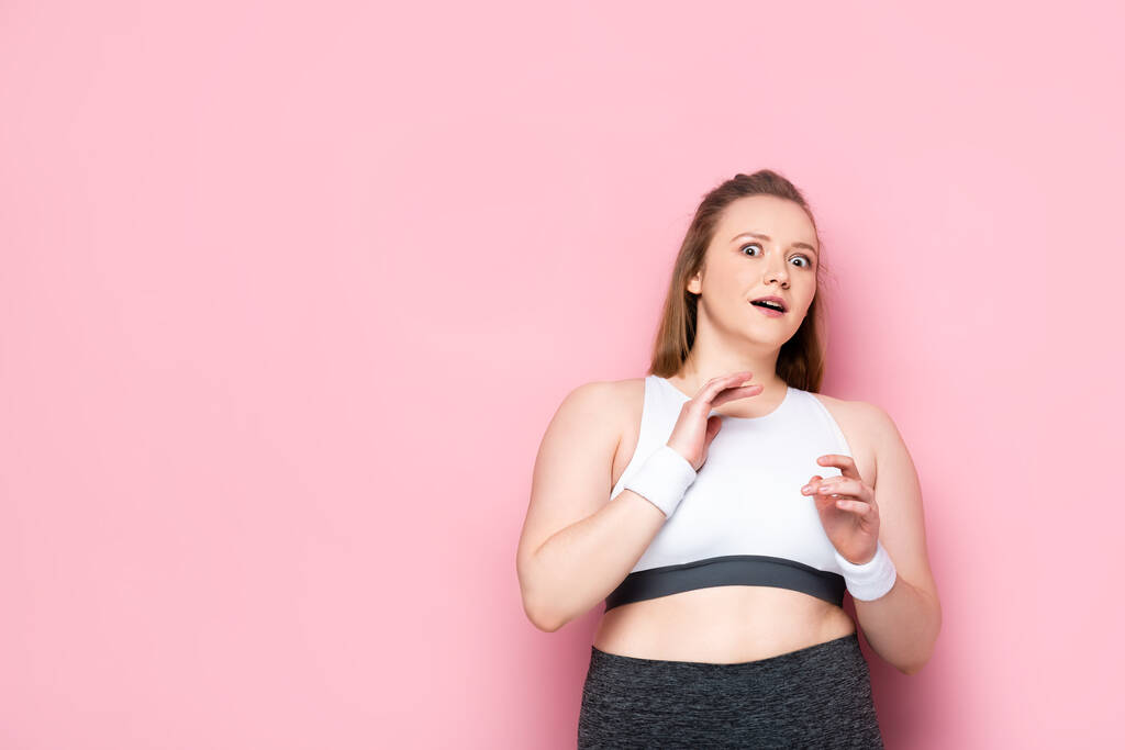 verängstigtes übergewichtiges Mädchen gestikuliert, während es in die Kamera auf rosa schaut - Foto, Bild