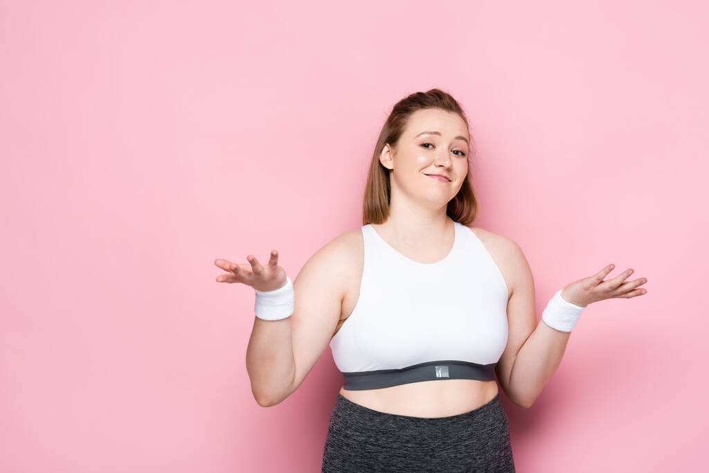 σύγχυση υπέρβαρο κορίτσι σε αθλητικά που δείχνει shrug χειρονομία σε ροζ - Φωτογραφία, εικόνα