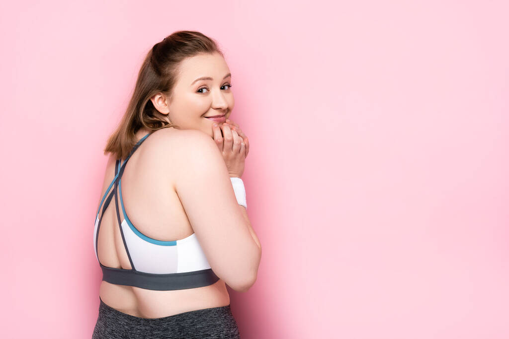 cheerful overweight girl touching chin while looking at camera on pink - Photo, Image