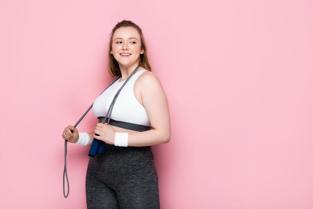 smiling overweight girl with jumping rope around neck looking away on pink - Photo, Image