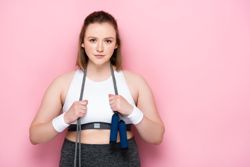 confident overweight girl with jumping rope around neck smiling at camera on pink - Photo, Image
