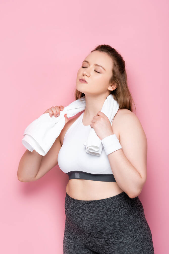 pretty overweight girl with closed eyes wiping neck with white towel on pink - Photo, Image