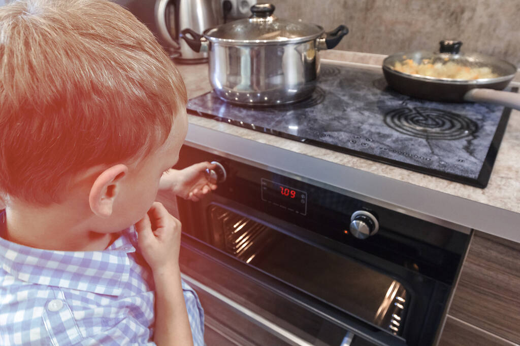 Περίεργο αγόρι που παίζει με πόμολα στο καμμένο φούρνο. Κίνδυνος για τα παιδιά στην κουζίνα. Ανασφαλής στο σπίτι, ατύχημα. Ζεστός φούρνος - Φωτογραφία, εικόνα