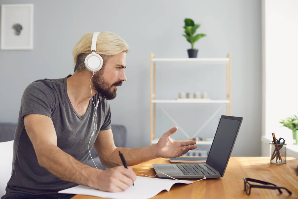 Werken vanuit huis of online onderwijs. Aantrekkelijke zakenman in headset met webconferentie op laptop op het werk - Foto, afbeelding
