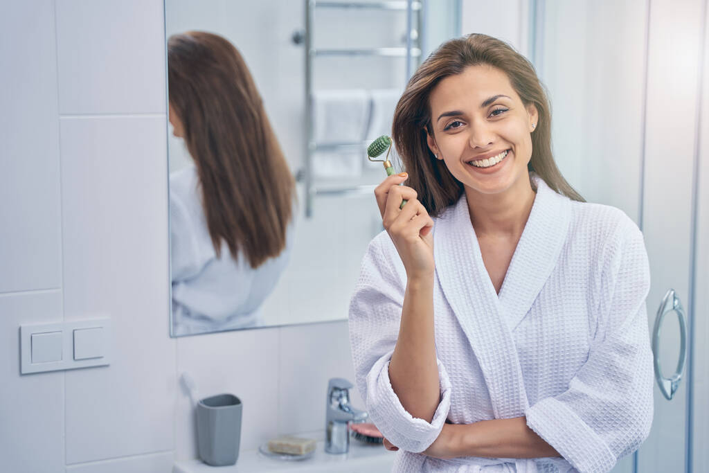 Attraktive junge Frau benutzt Gesichtsmassagegerät im Badezimmer - Foto, Bild