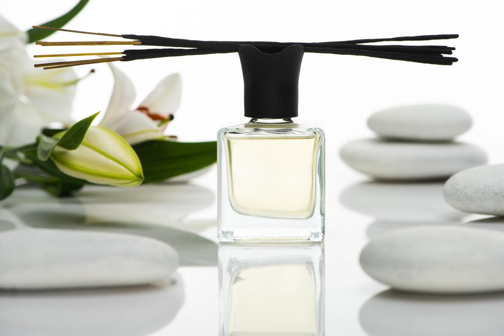 selektivní zaměření vonných tyčinek a parfémů v blízkosti lázeňských kamenů a lilií izolovaných na bílém - Fotografie, Obrázek
