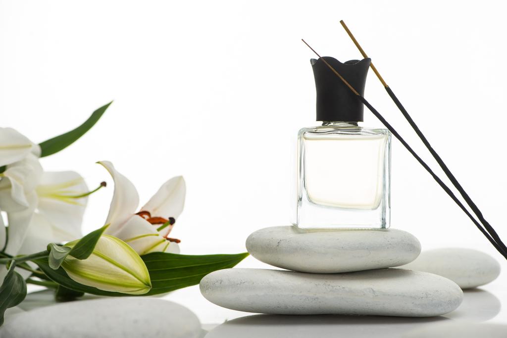 aromatyczne paluszki i perfumy na kamieniach uzdrowiskowych w pobliżu lilii wyizolowanych na białym - Zdjęcie, obraz