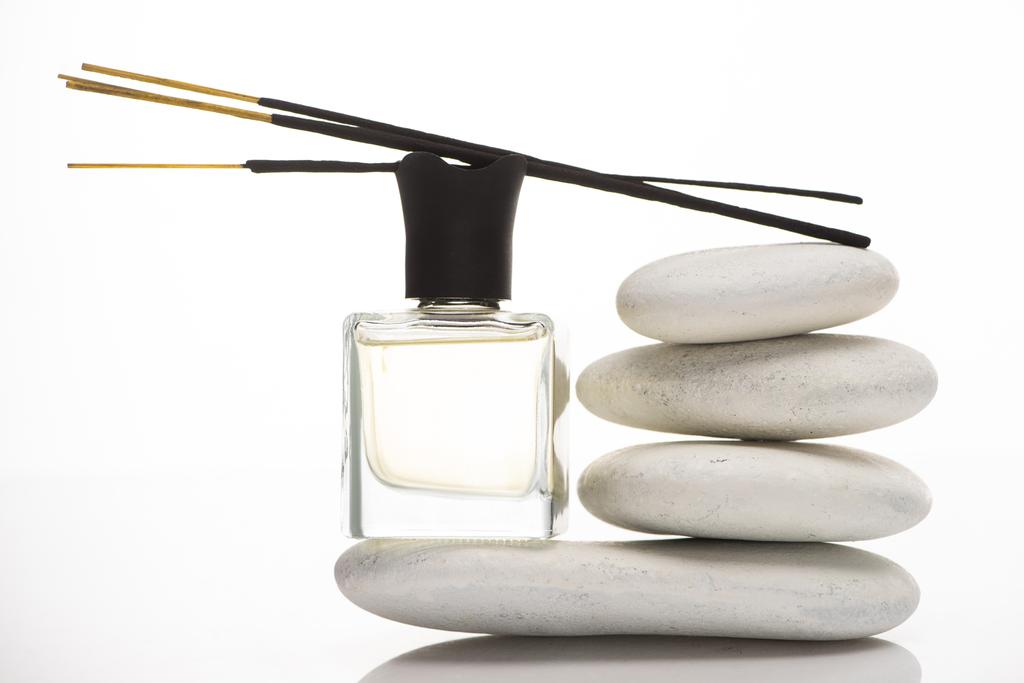 varas de aroma no perfume em garrafa perto de pedras de spa no fundo branco
 - Foto, Imagem