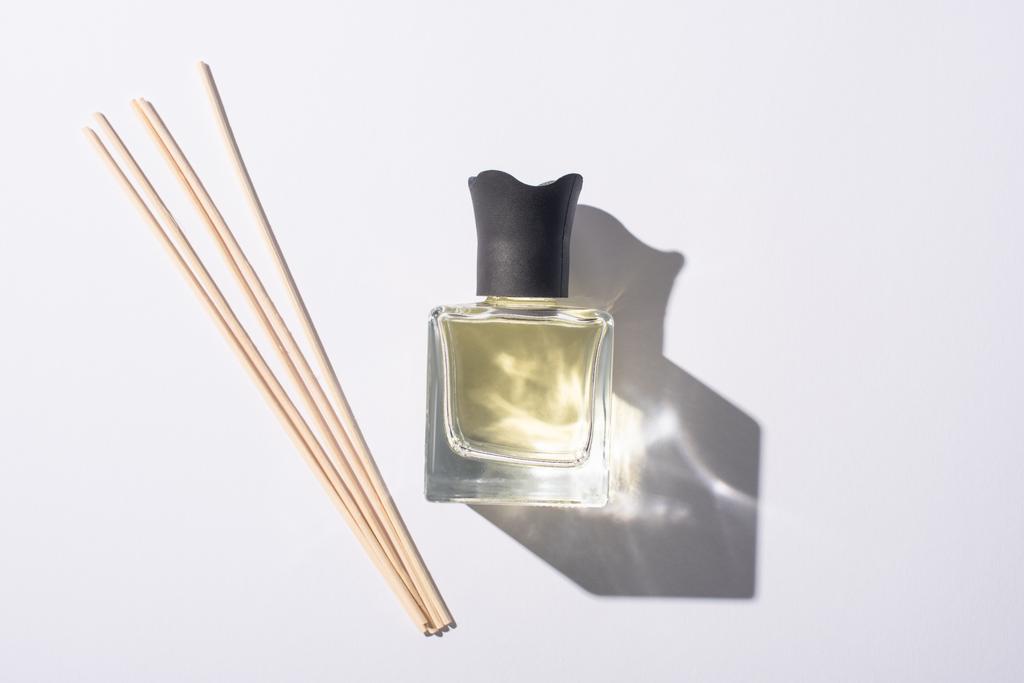 vista superior de varas de aroma perto de perfume em garrafa no fundo branco
 - Foto, Imagem