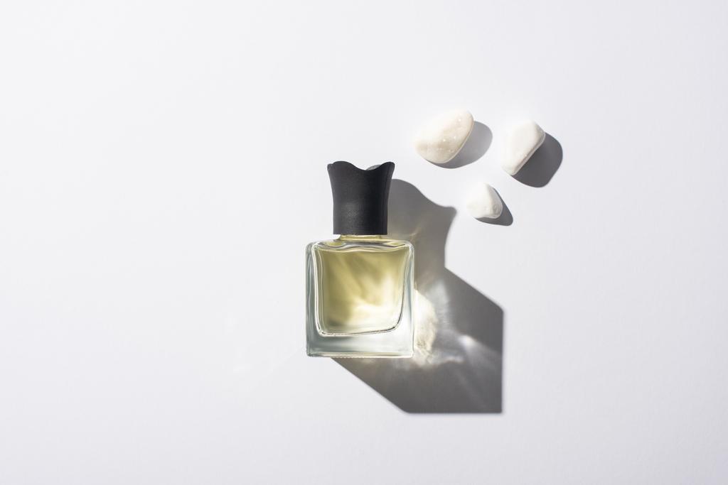 vista superior del perfume casero en botella cerca de piedras sobre fondo blanco
 - Foto, imagen