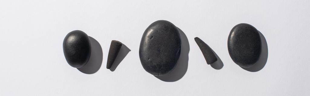 vista superior de conos de incienso negro y piedras de spa sobre fondo blanco, plano panorámico
 - Foto, Imagen