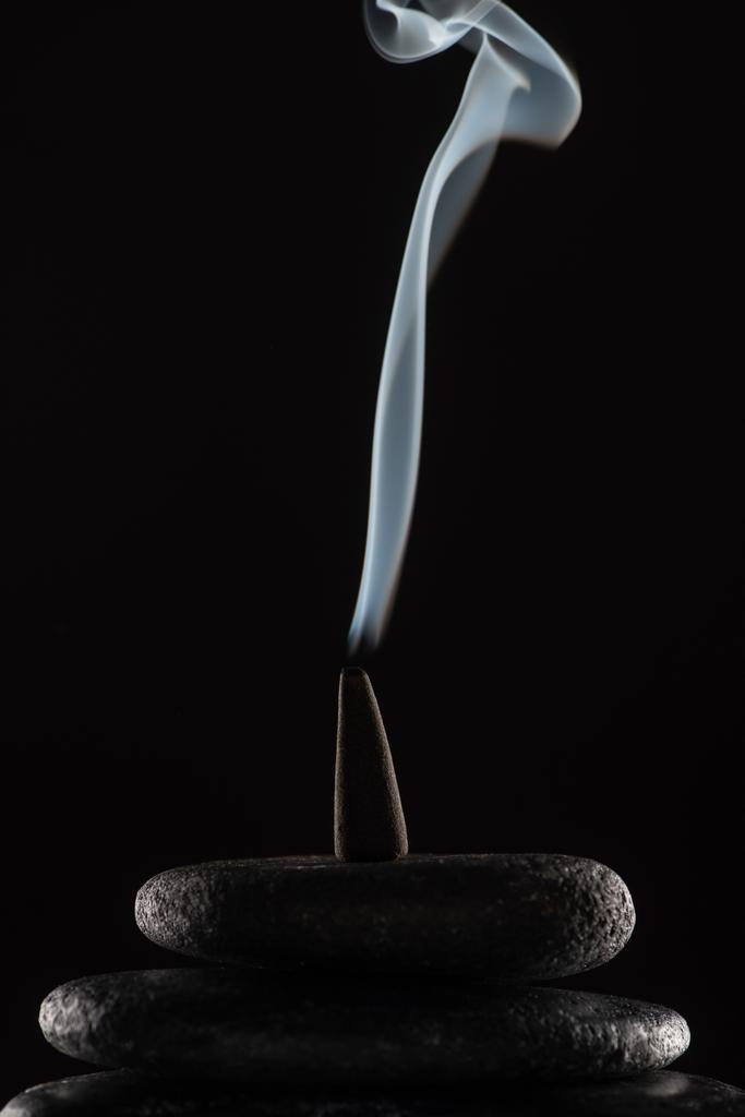 cône d'encens brûlant avec de la fumée sur des pierres sur fond noir - Photo, image
