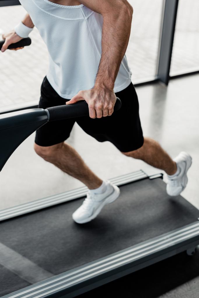cropped view of tired sportsman touching handrails on treadmill  - Photo, Image